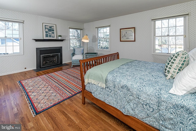 bedroom with a fireplace with flush hearth, multiple windows, wallpapered walls, and wood finished floors