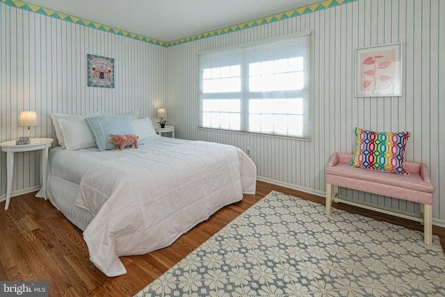 bedroom with baseboards, wood finished floors, and wallpapered walls