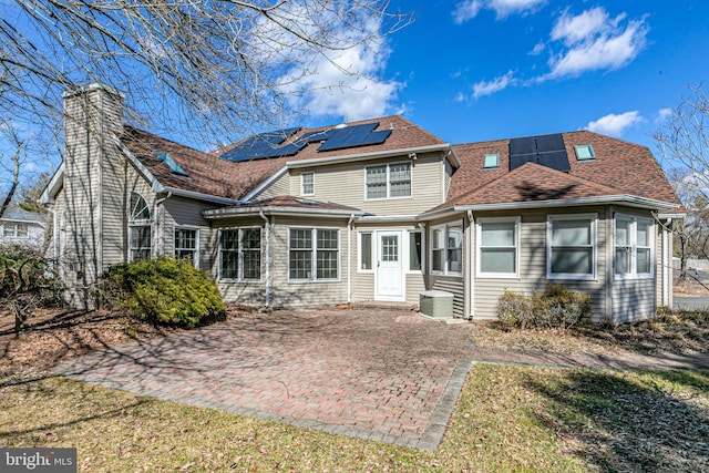 rear view of house with roof mounted solar panels, a chimney, and a shingled roof