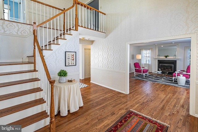 staircase with a wainscoted wall, wallpapered walls, a high ceiling, and wood finished floors