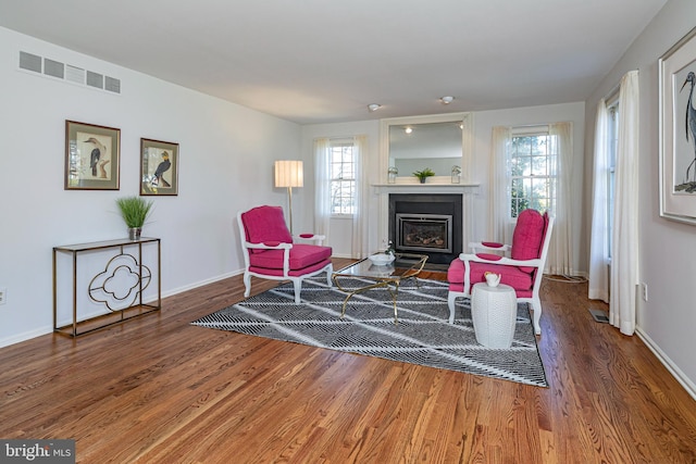 living area featuring visible vents, a fireplace with flush hearth, baseboards, and wood finished floors