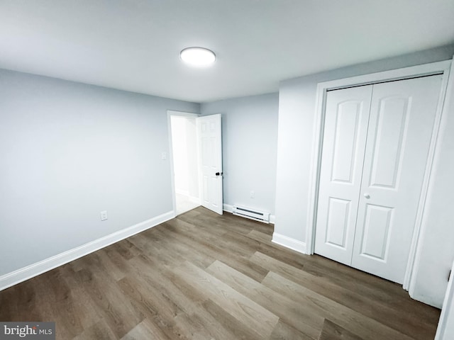 unfurnished bedroom with a closet, a baseboard heating unit, baseboards, and wood finished floors