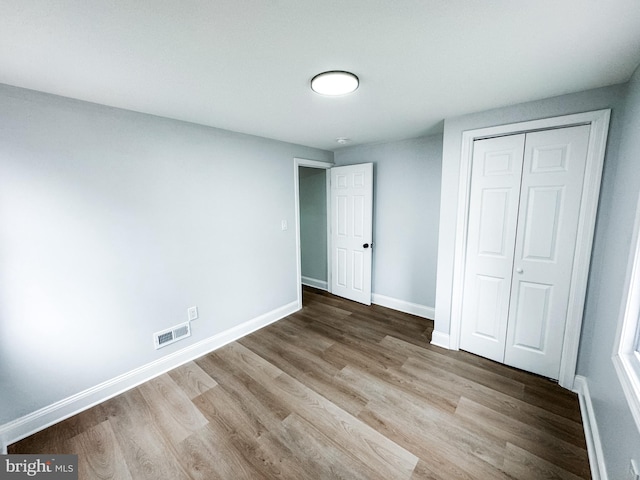 unfurnished bedroom featuring a closet, visible vents, baseboards, and wood finished floors