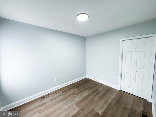 unfurnished bedroom featuring visible vents, baseboards, a closet, and dark wood finished floors