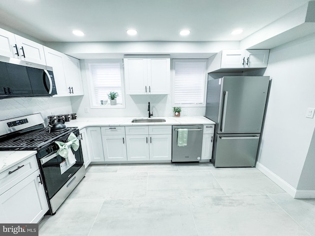 kitchen with light stone countertops, baseboards, a sink, stainless steel appliances, and white cabinets