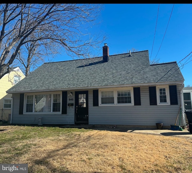 view of front of home featuring a chimney, a front lawn, and a shingled roof