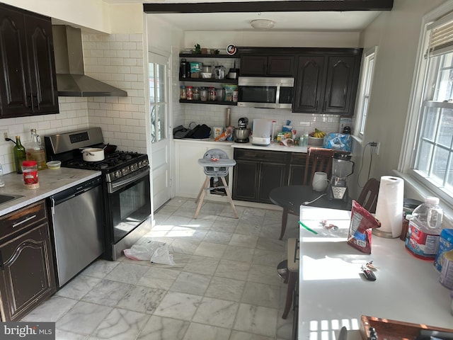 kitchen with backsplash, appliances with stainless steel finishes, light countertops, and wall chimney range hood