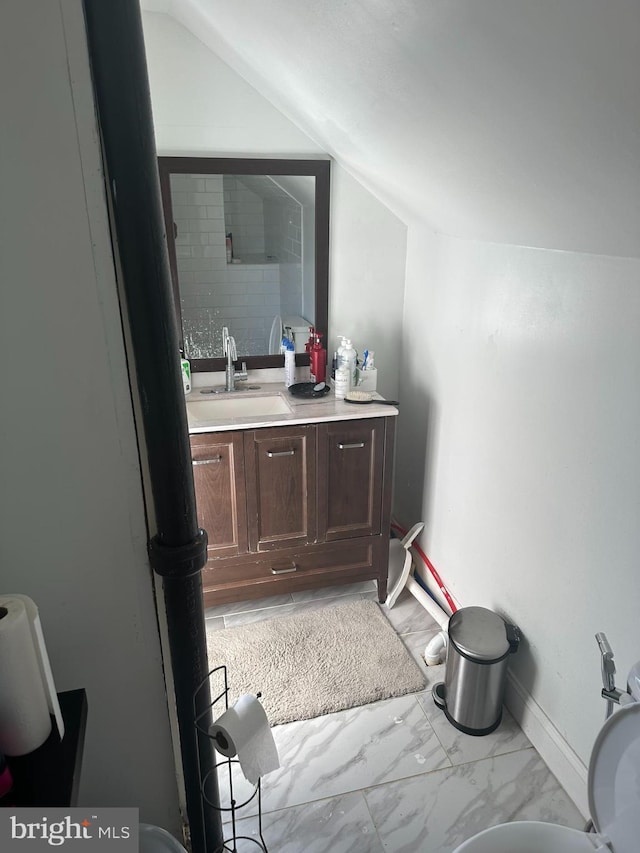 bathroom featuring marble finish floor, baseboards, vanity, and lofted ceiling