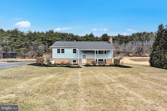 raised ranch with a chimney, a front yard, a trampoline, and brick siding