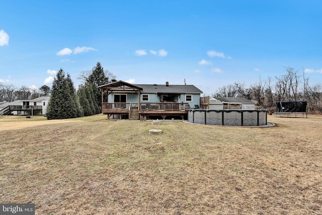 back of property with a covered pool, a trampoline, a lawn, and a wooden deck