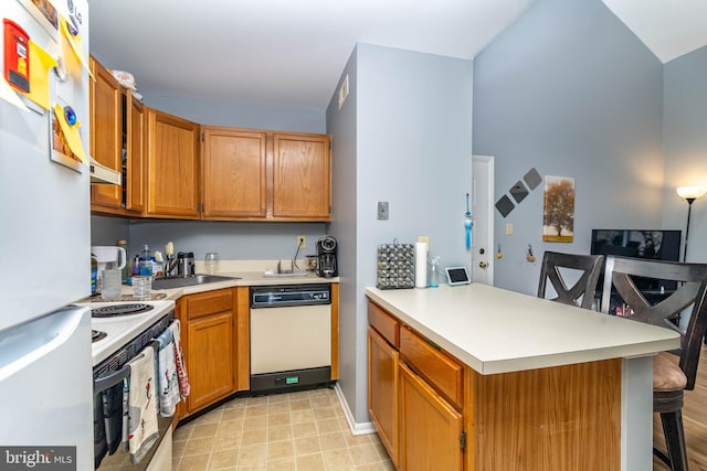 kitchen featuring a kitchen bar, white appliances, a peninsula, and light countertops