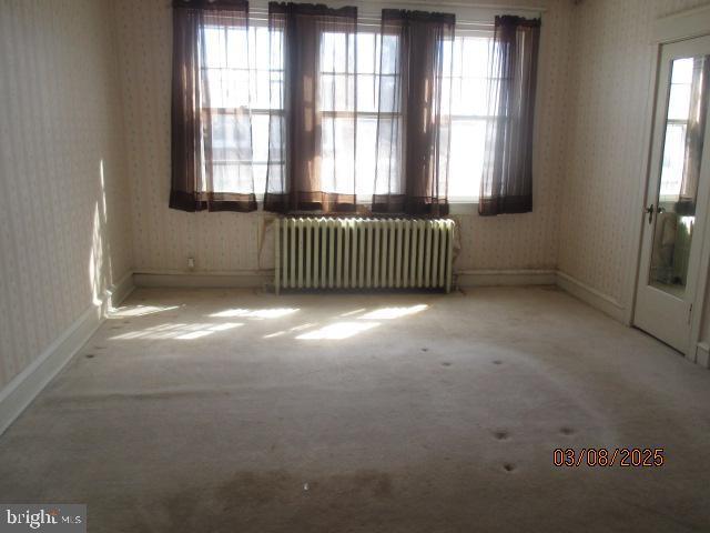 carpeted spare room featuring wallpapered walls, radiator, and a wealth of natural light