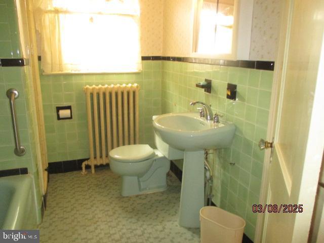 bathroom featuring toilet, a washtub, radiator, wainscoting, and wallpapered walls