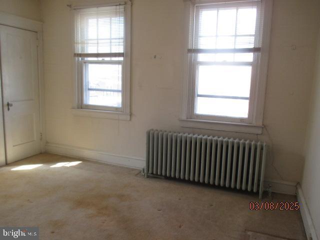 unfurnished room featuring radiator, baseboards, and carpet floors