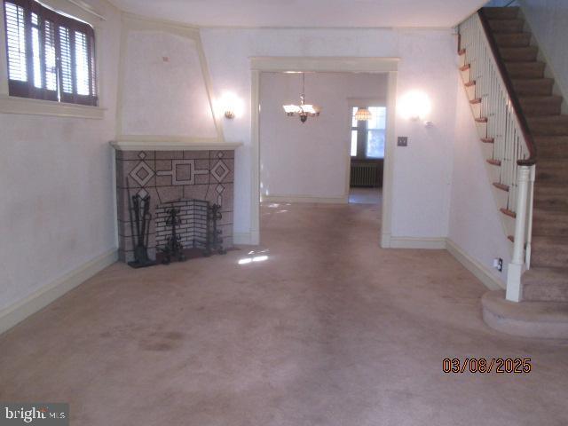 unfurnished living room featuring a wealth of natural light, stairway, radiator, and an inviting chandelier