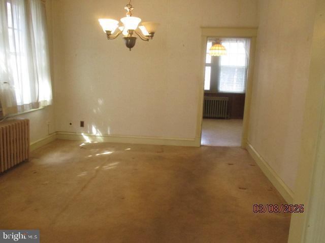 unfurnished room featuring an inviting chandelier, radiator heating unit, and baseboards