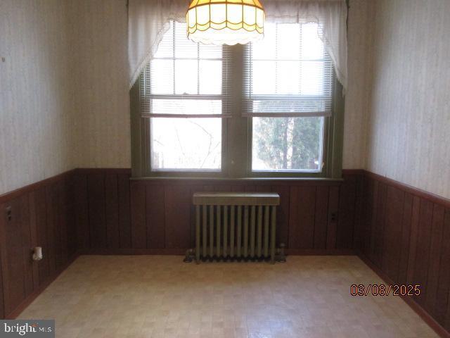 empty room featuring wallpapered walls, radiator, a wainscoted wall, and plenty of natural light