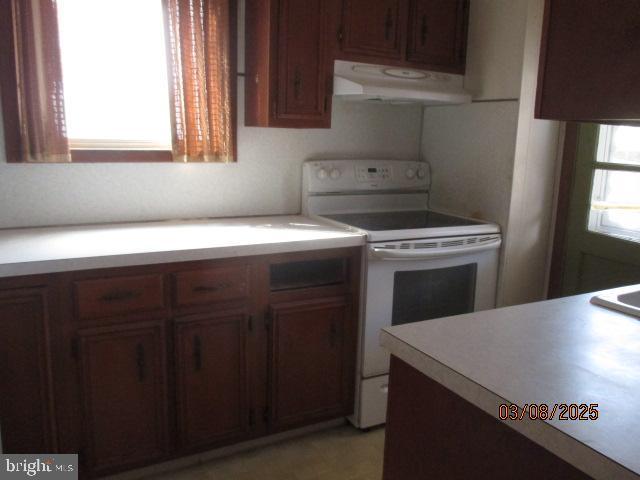 kitchen featuring light countertops, brown cabinetry, under cabinet range hood, and white electric stove