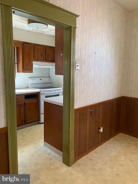 kitchen with electric range, light floors, ventilation hood, and a wainscoted wall