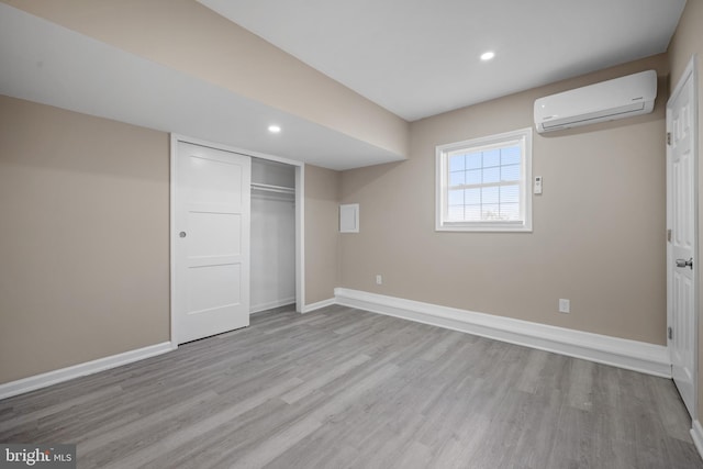 unfurnished bedroom featuring wood finished floors, a wall unit AC, recessed lighting, a closet, and baseboards