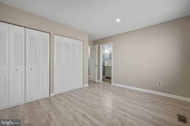 unfurnished bedroom with baseboards, visible vents, ensuite bath, light wood-style flooring, and multiple closets