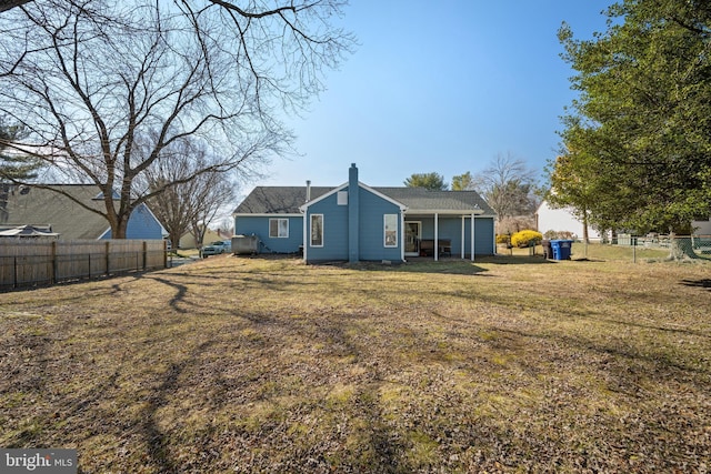 back of house featuring a lawn, a chimney, and fence