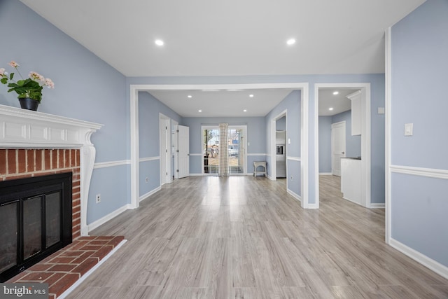 unfurnished living room with a brick fireplace, light wood-type flooring, and baseboards