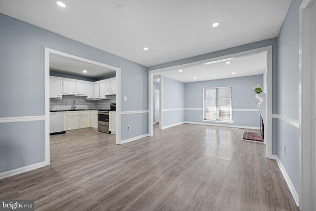 kitchen featuring white dishwasher, stainless steel range with electric stovetop, light wood-style floors, open floor plan, and backsplash