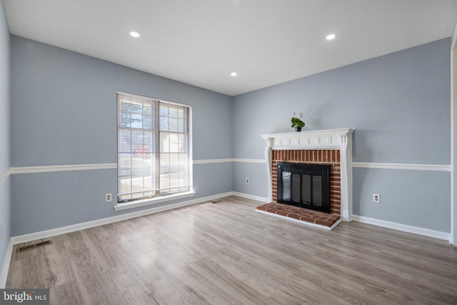 unfurnished living room with wood finished floors, visible vents, baseboards, recessed lighting, and a brick fireplace