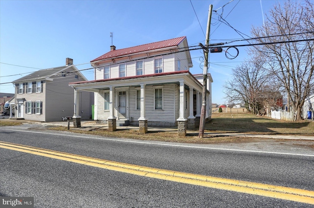 view of front of home featuring a porch, fence, a chimney, and metal roof