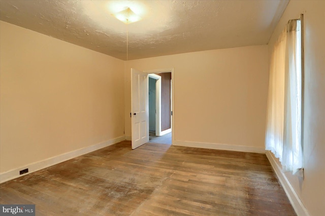 empty room with a textured ceiling, baseboards, and wood finished floors