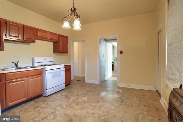 kitchen featuring white gas stove, a sink, decorative light fixtures, light countertops, and baseboards