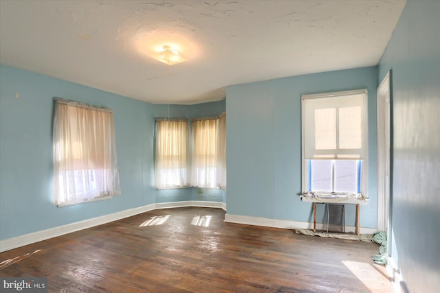 spare room featuring dark wood-type flooring and baseboards