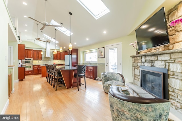 interior space featuring a ceiling fan, vaulted ceiling with skylight, recessed lighting, a fireplace, and light wood-style floors