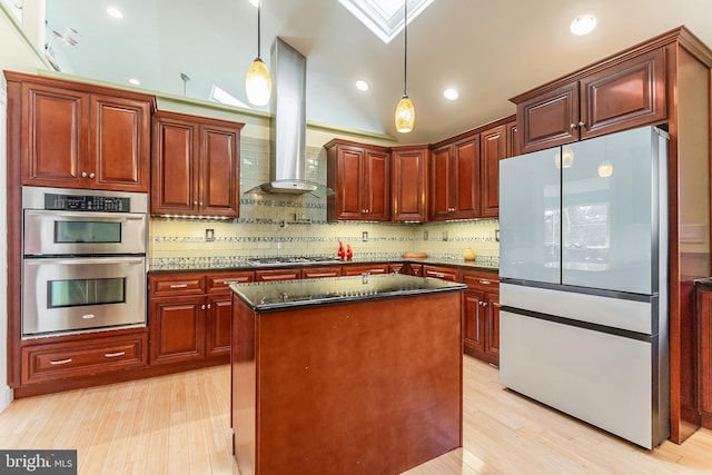 kitchen featuring tasteful backsplash, pendant lighting, light wood-style flooring, appliances with stainless steel finishes, and wall chimney exhaust hood