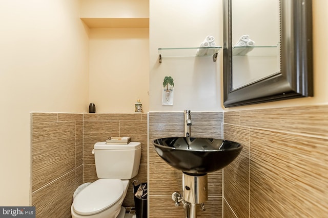 half bath featuring a sink, toilet, tile walls, and wainscoting