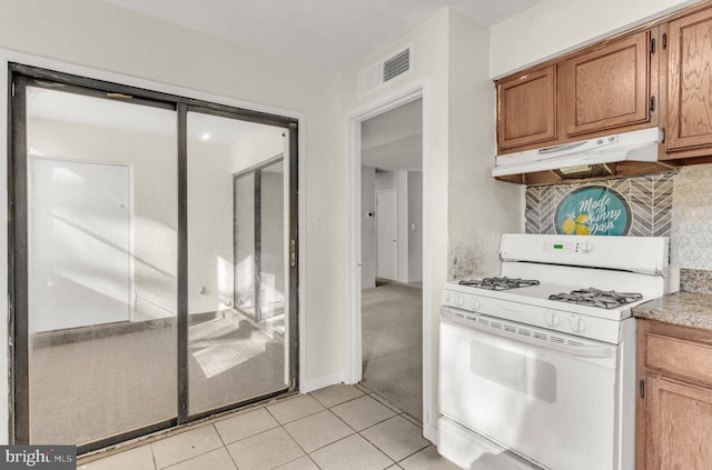 kitchen featuring visible vents, brown cabinets, white gas stove, under cabinet range hood, and backsplash