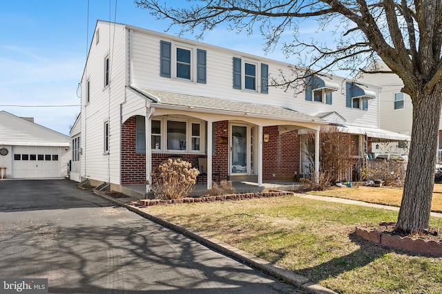 view of front facade featuring brick siding, covered porch, an outdoor structure, a garage, and driveway