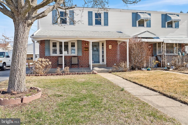 view of front of property featuring brick siding, covered porch, a front lawn, and roof with shingles