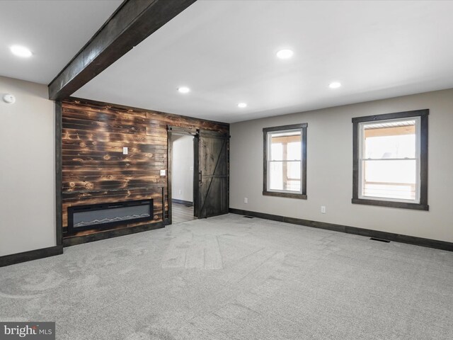 unfurnished living room with visible vents, wooden walls, beamed ceiling, a barn door, and carpet flooring