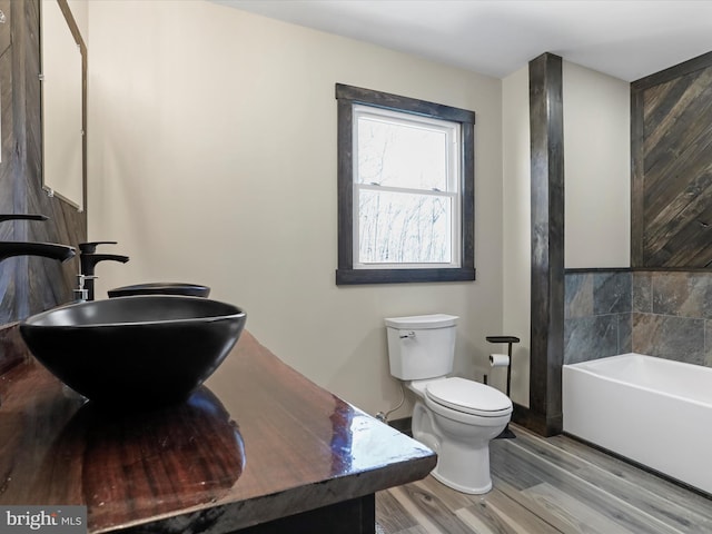 bathroom with a bath, wood finished floors, toilet, and a sink