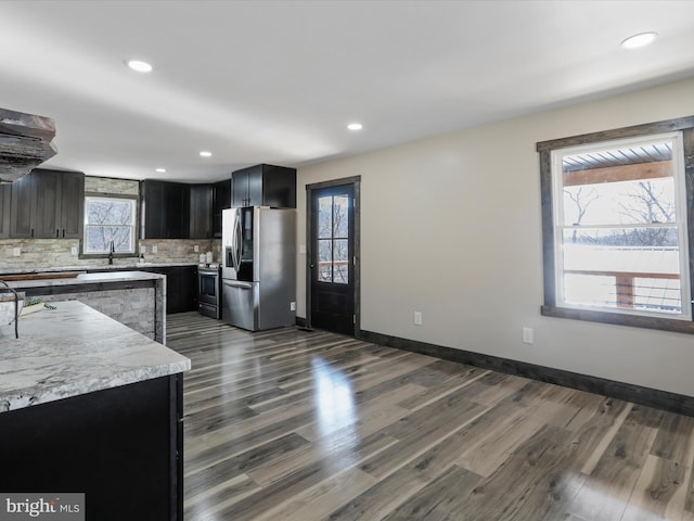 kitchen with dark wood-type flooring, dark cabinetry, stainless steel appliances, decorative backsplash, and baseboards