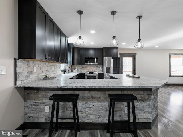 kitchen featuring a sink, hanging light fixtures, dark wood-type flooring, appliances with stainless steel finishes, and tasteful backsplash