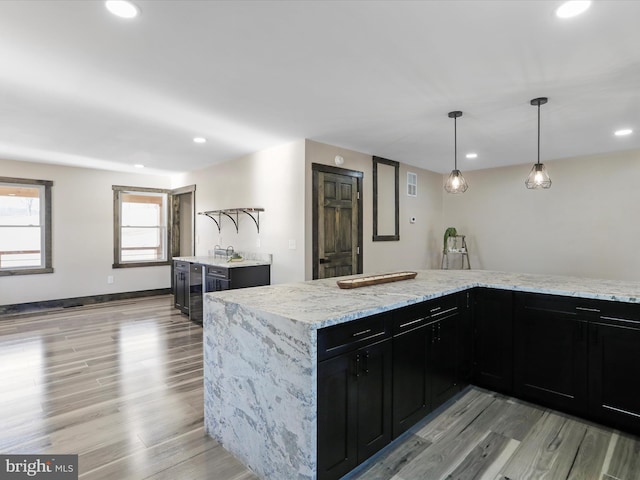 kitchen featuring light stone counters, light wood-style floors, dark cabinets, and recessed lighting