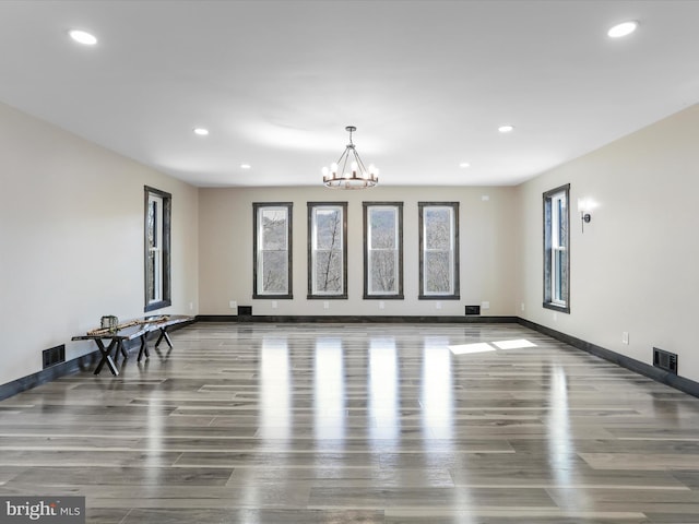 interior space with a notable chandelier, visible vents, baseboards, and wood finished floors