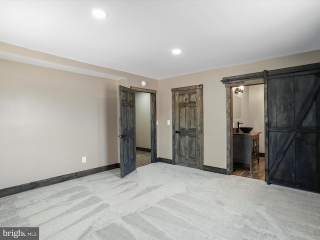 unfurnished bedroom featuring a barn door, recessed lighting, carpet, and baseboards