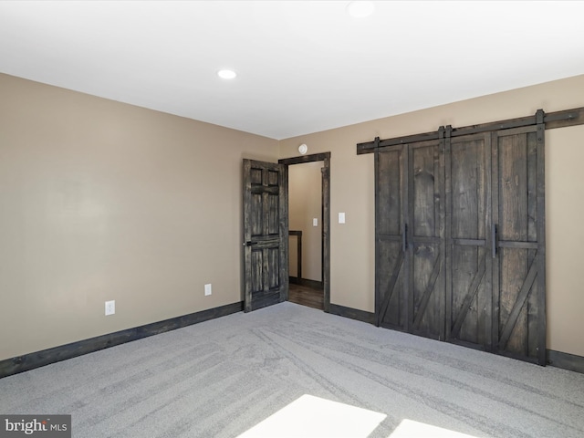 unfurnished bedroom featuring recessed lighting, baseboards, carpet, and a barn door