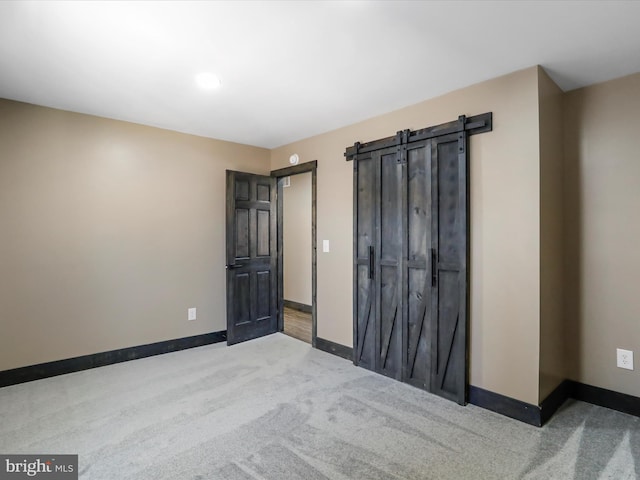 unfurnished bedroom with a barn door, carpet, and baseboards