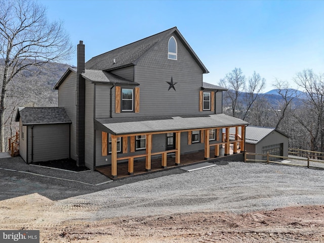 rear view of house with a porch, a chimney, an outdoor structure, and roof with shingles