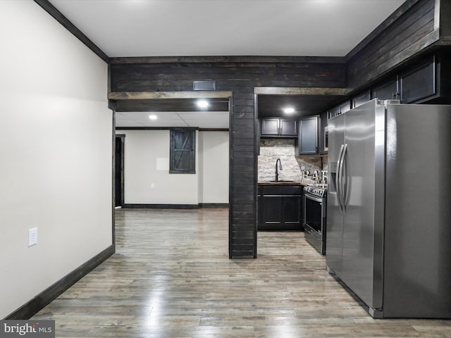 kitchen with baseboards, light wood finished floors, a sink, appliances with stainless steel finishes, and tasteful backsplash